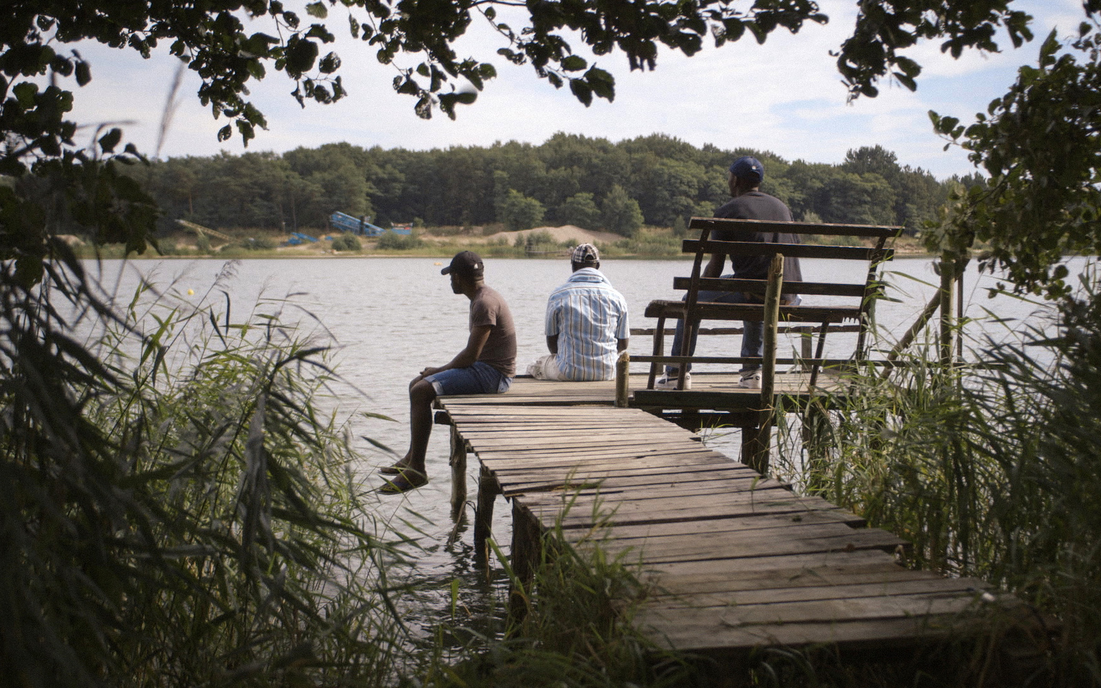 Three men sitting on a pier at a lake