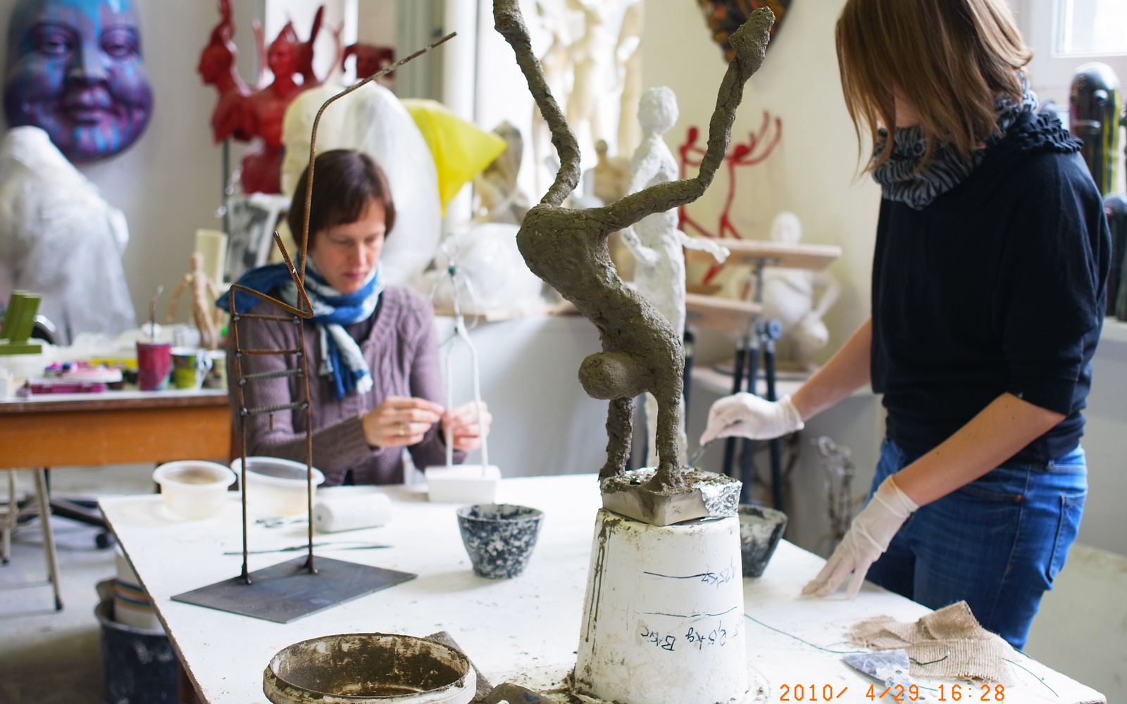 Women in an atelier are workig on slender figurines out of gesso.