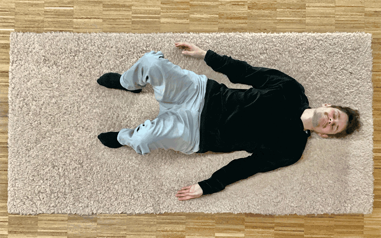 Max Kosoric ist liegend auf einem Teppich von oben zu sehen wie er seine angestellten Beine nach links neigt.