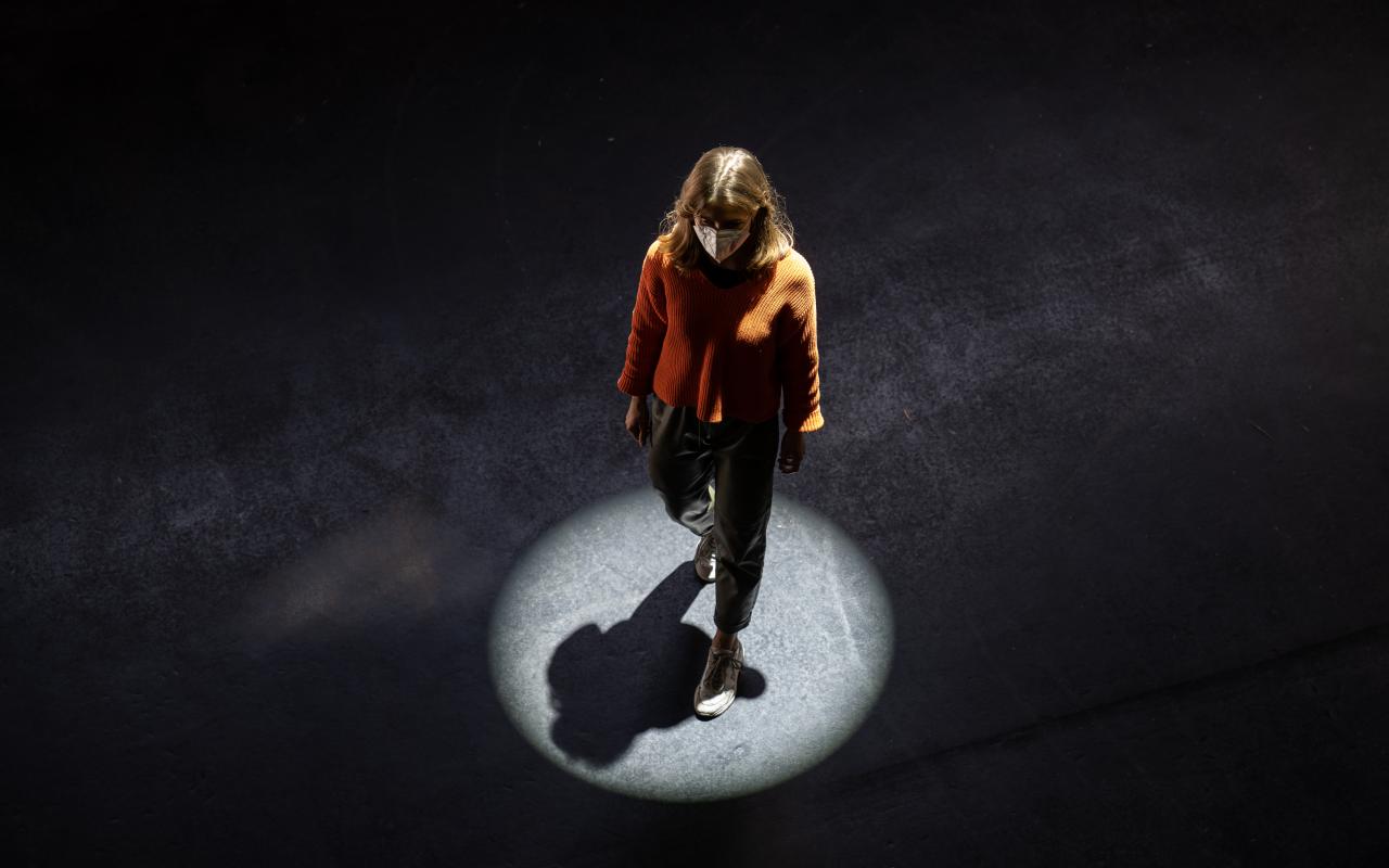 You can see a woman walking across a black floor, illuminated by a circular spotlight. 