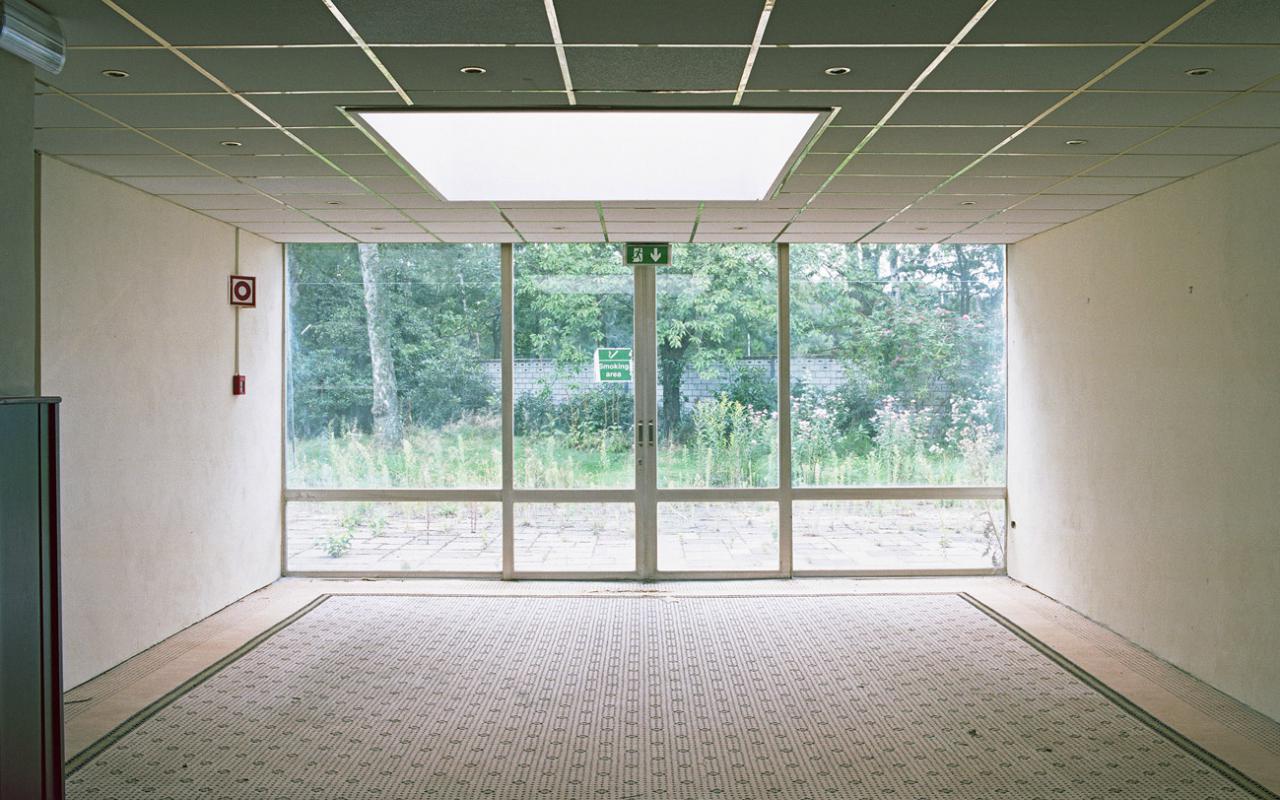 Ein leerer Raum mit großen Fensterfront mit Blick in einen begrünten Außenbereich.