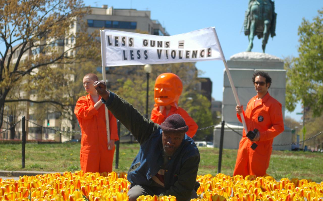 A man in the flower bed raises his right fist as a sign of protest. Behind him, three men with a banner.