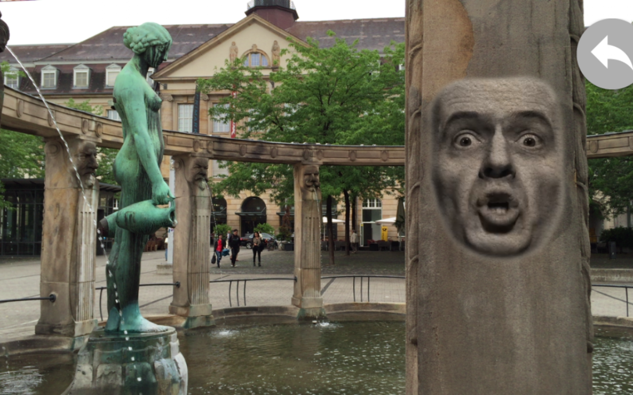 Blick auf den Stephanienbrunnen am Stephansplatz: auf der Säule ist die Projektion eines sprechenden, männlichen Gesichts zu sehen.