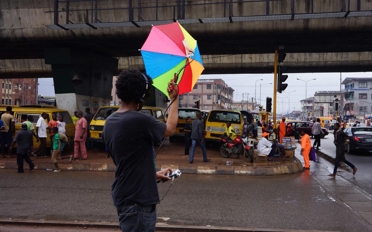 A man with a colorful umbrella records ambient noise on a busy street