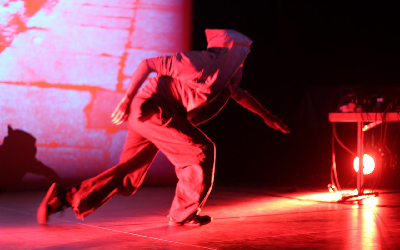A man on stage with hooded jacket dipped in red light
