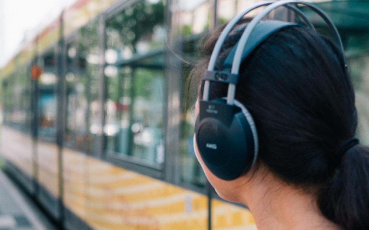 Eine Frau mit Kopfhörern und Handy vor einer Straßenbahn