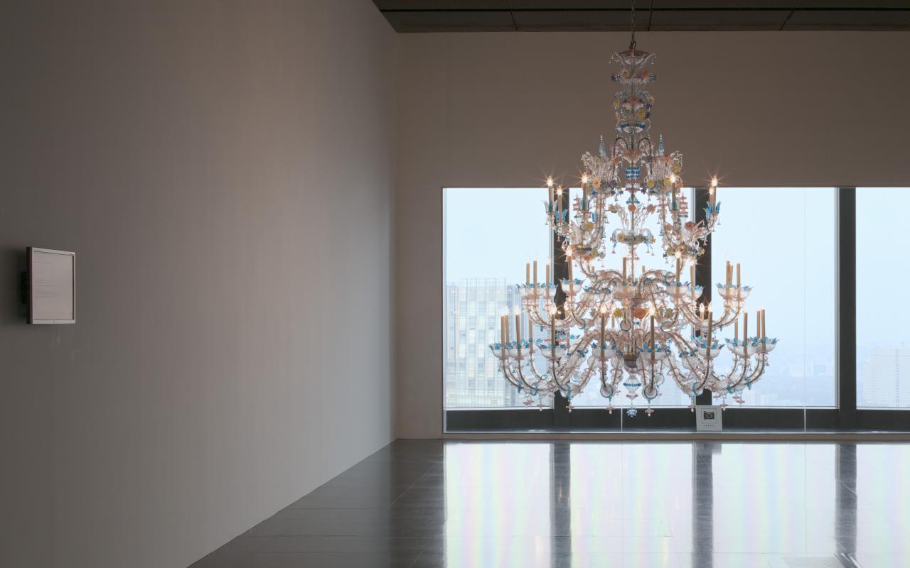 Illuminated chandelier in empty room in front of large windows.