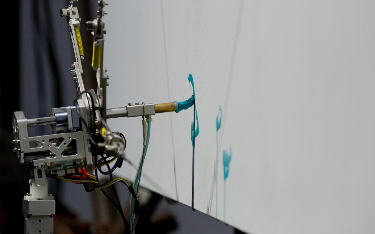 Das Bild zeigt einen robotergesteuerten Pinsel, der türkisfarbene Farbe auf eine weiße Leinwand aufträgt. 
