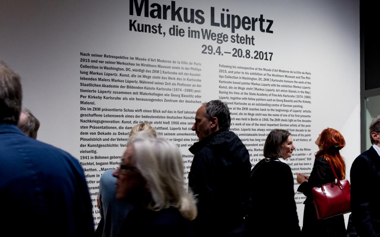 The picture shows visitors in front of an information board for Markus Lüpertz