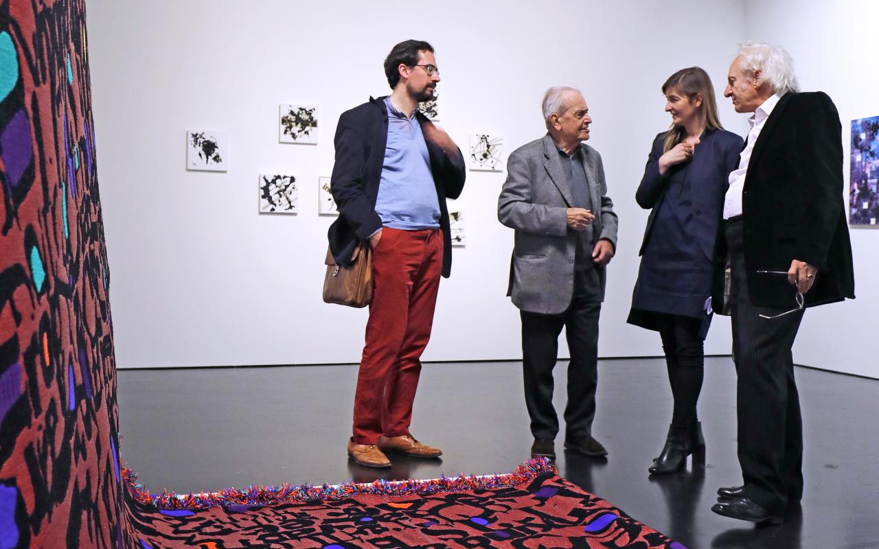Vier Menschen stehen vor einem Werk, das aus einem langen roten Teppich mit Buchstaben besteht.