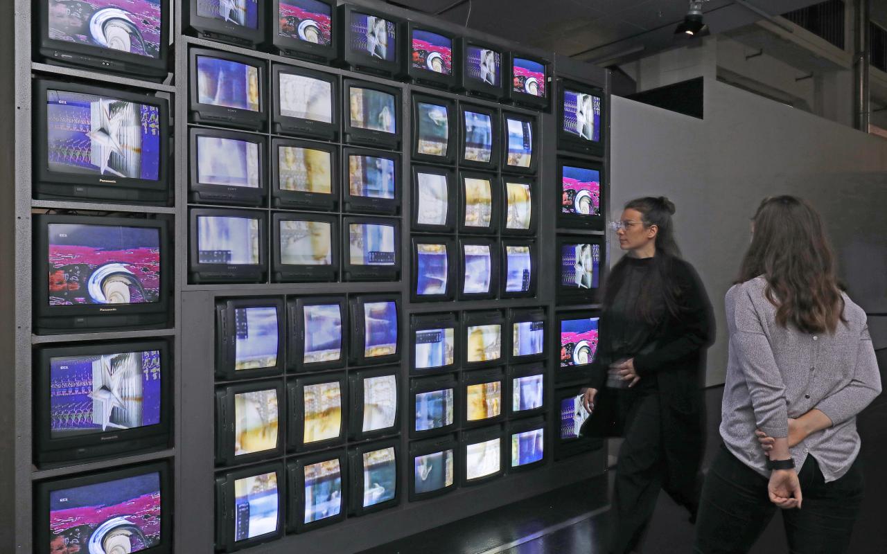 Visitors in front of an installation of 52 monitors, which show a colorful picture choreography.