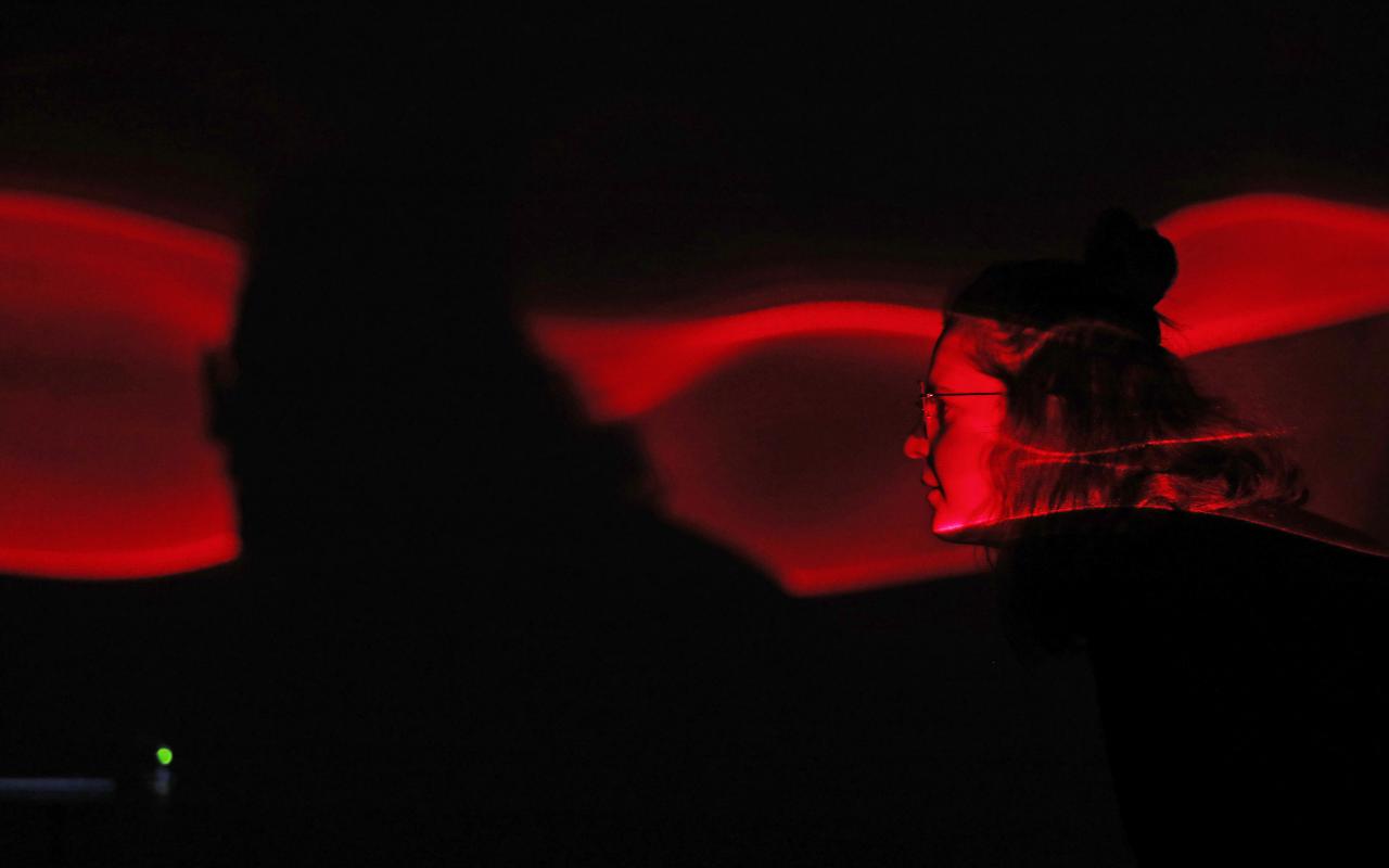  The face of a visitor is red-lit by a broken laser projection.