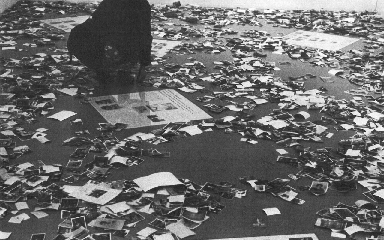 Die Schwarzweiß-Fotografie zeigt viele auf dem Boden zerstreute Fotos.