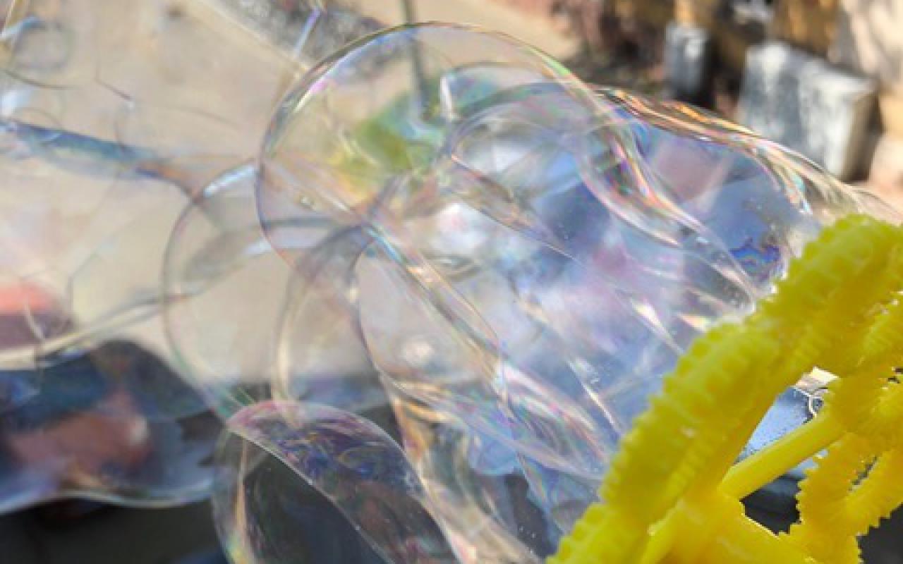 The wind blows many shimmering soap bubbles through a yellow bubble wheel.