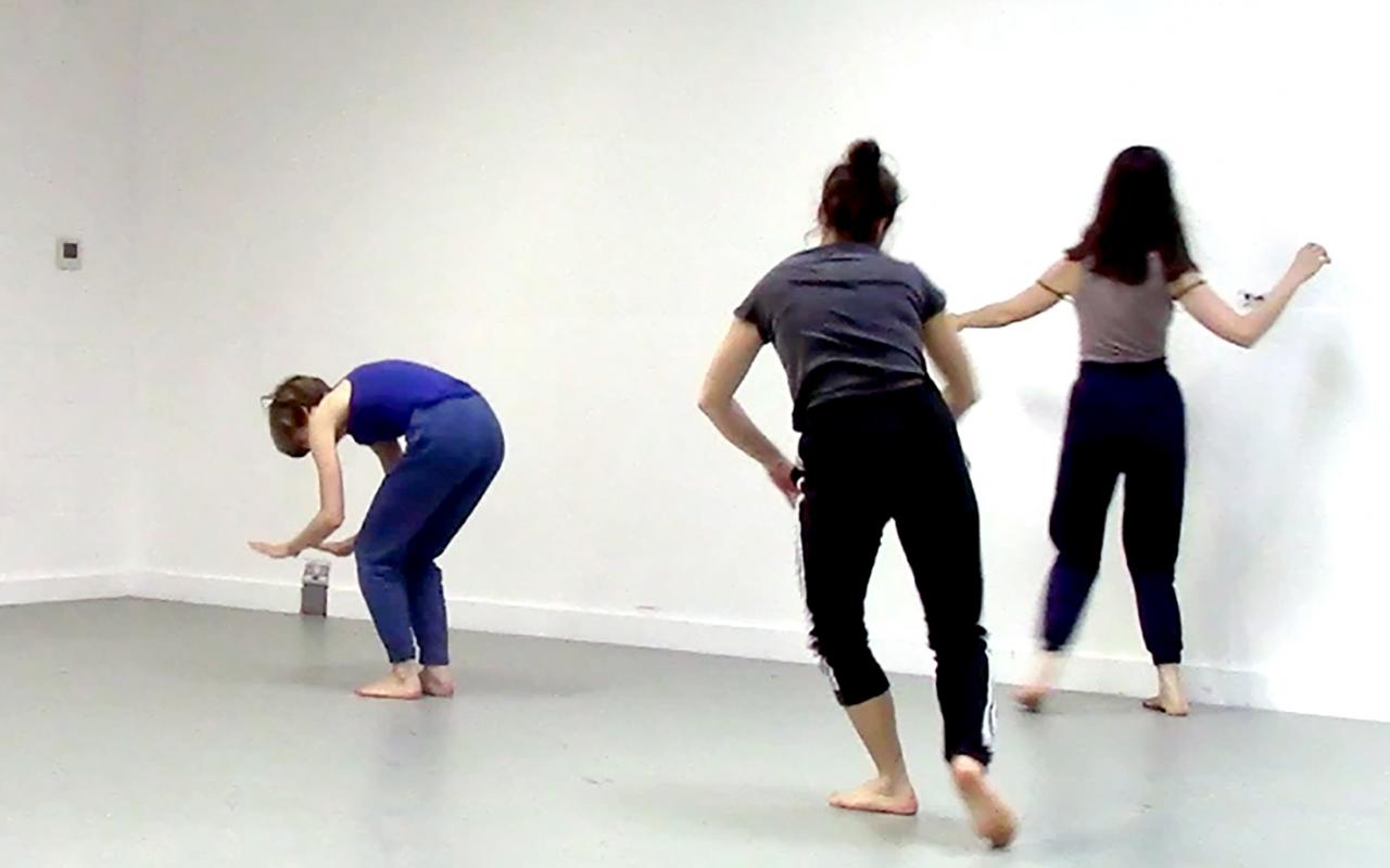 Zu sehen sind drei junge Frauen, die in tänzerischer Bewegung sich durch den Raum bewegen.