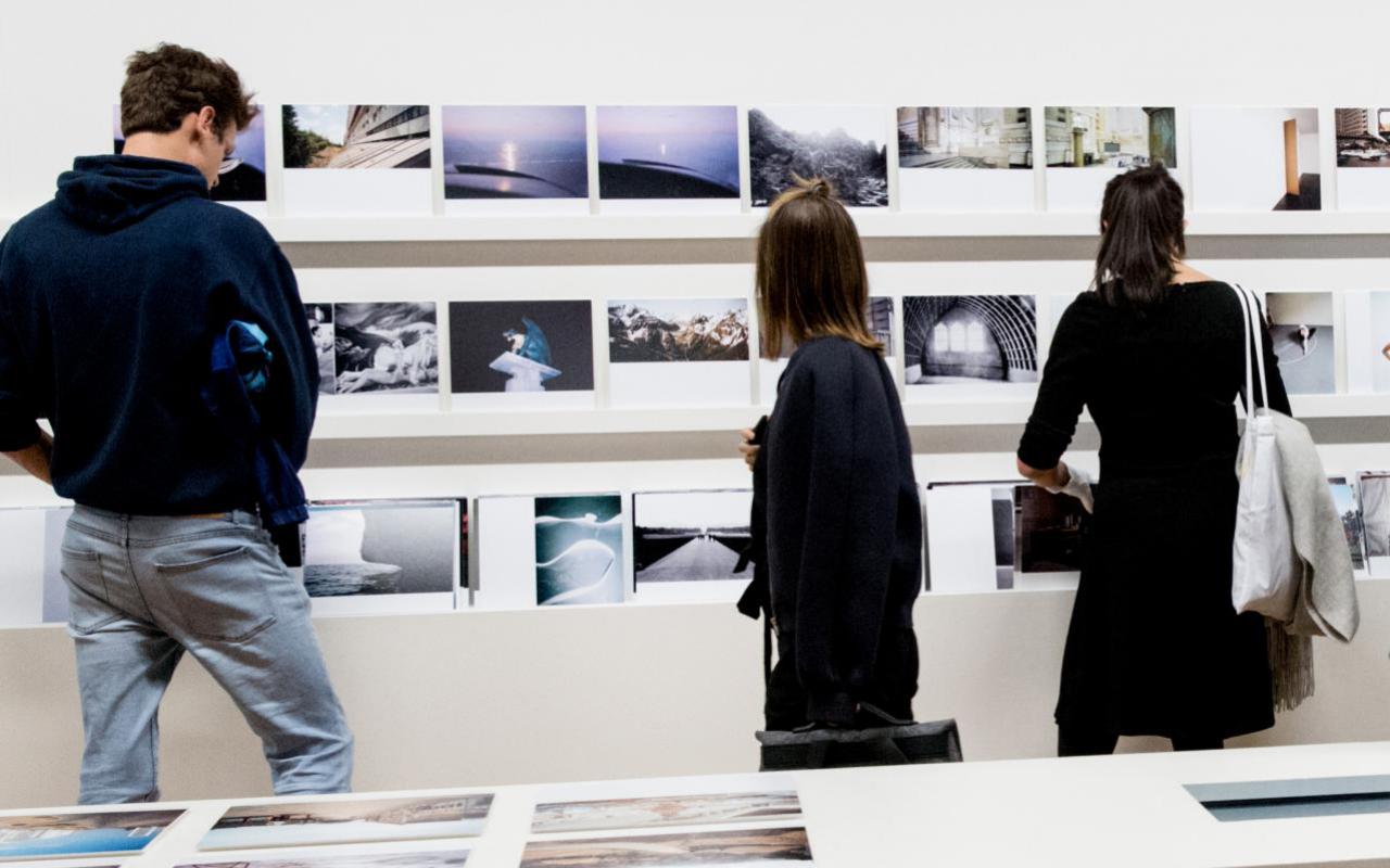 Three people view photographs in an exhibition