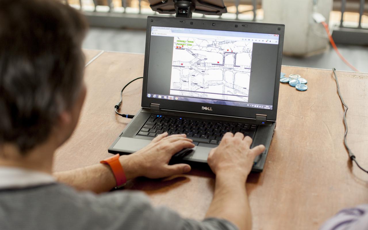 Ein Mann sitzt vor dem Laptop auf dem der Hintergrund eines Computerspiels gezeichnet ist.