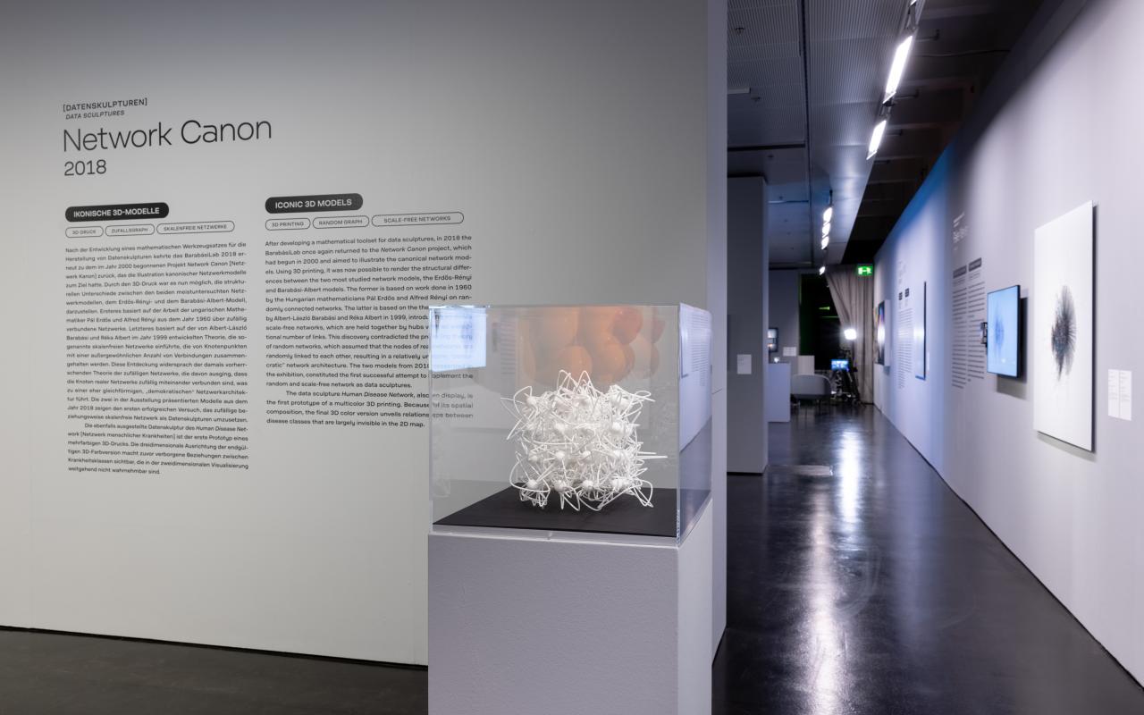 Ein Ausstellungsraum mit einem weißen 3D-Netzwerk-Modell in einem Glaskasten.