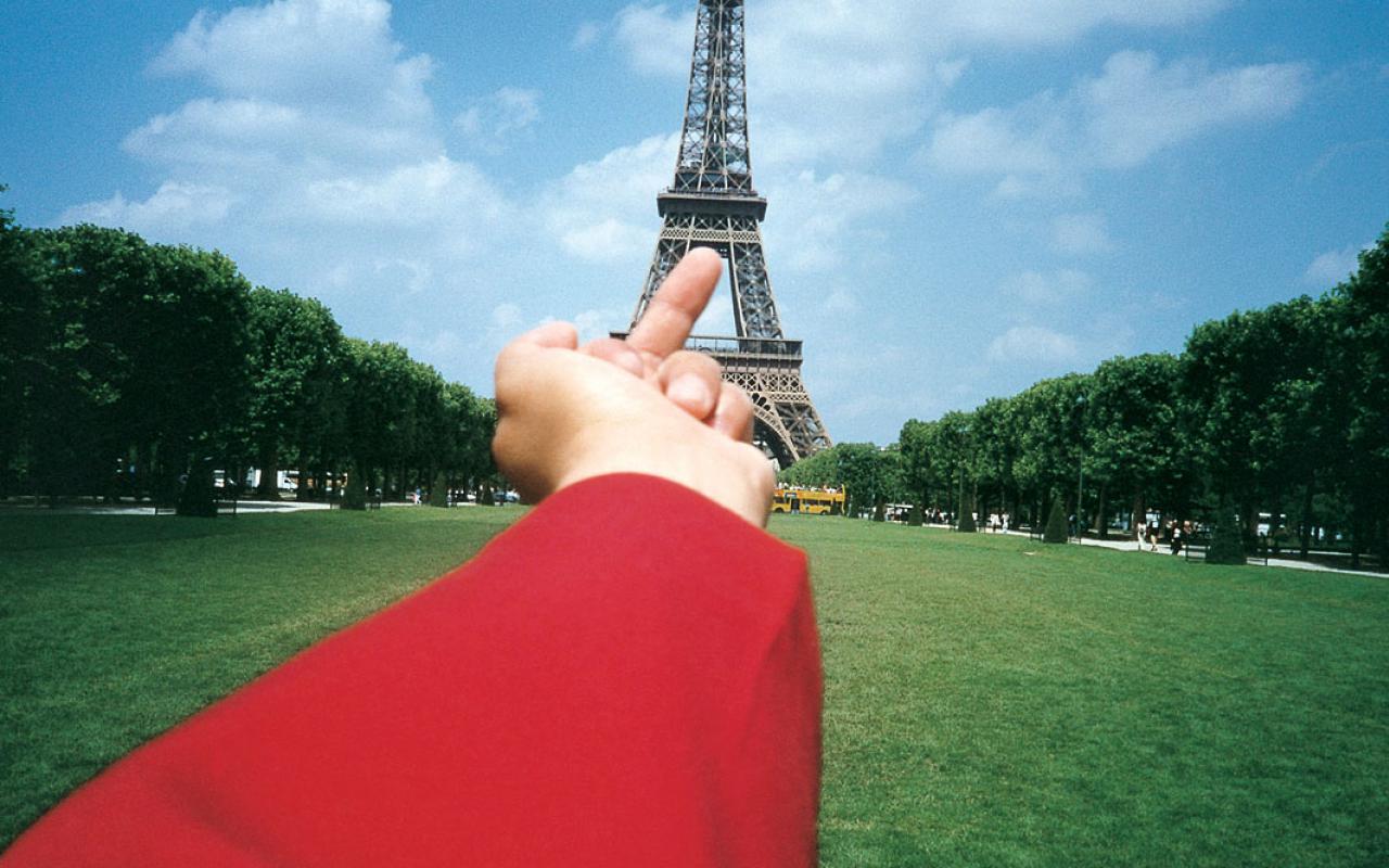 Zu sehen ist ein ausgestreckter roter Ärmel, der den Mittelfinger auf den Eiffelturm zeigt