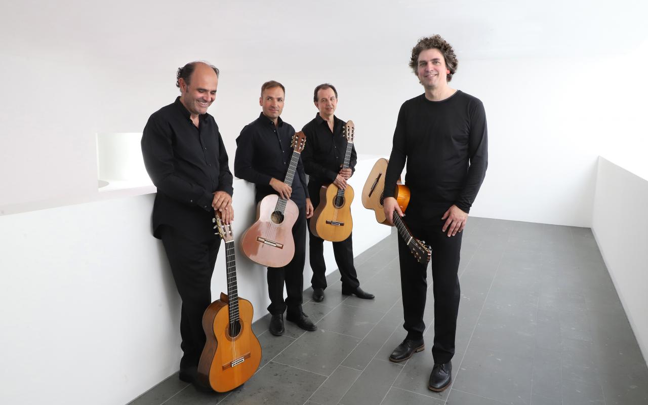 Auf dem Foto zu sehen, sind vier Männer, die in schwarz gekleidet sind und jeder hat eine Gitarre in seiner Hand. 