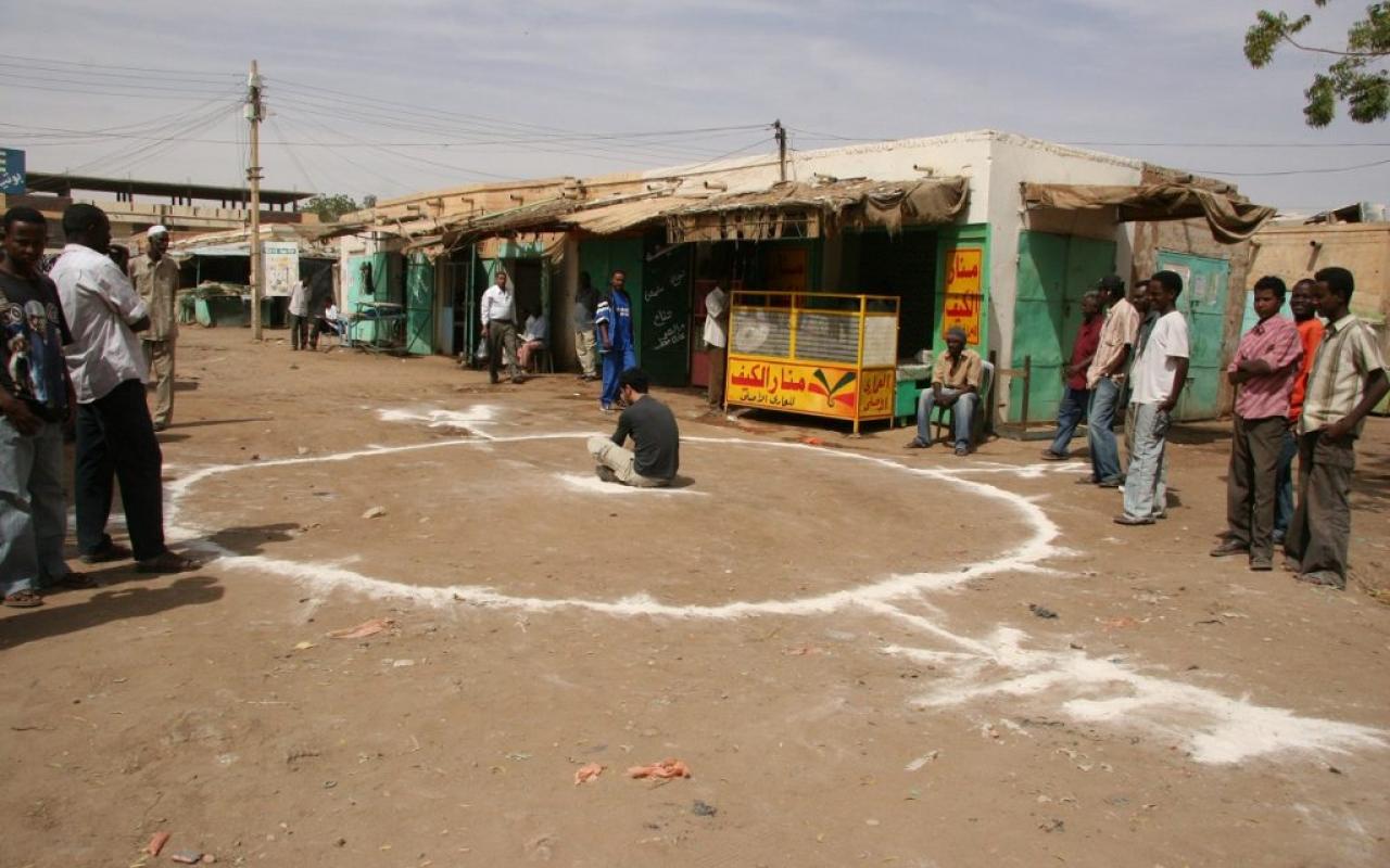 Artist Barış Seyitvan sits inside a white circle painted on the floor in a Sudanese village.