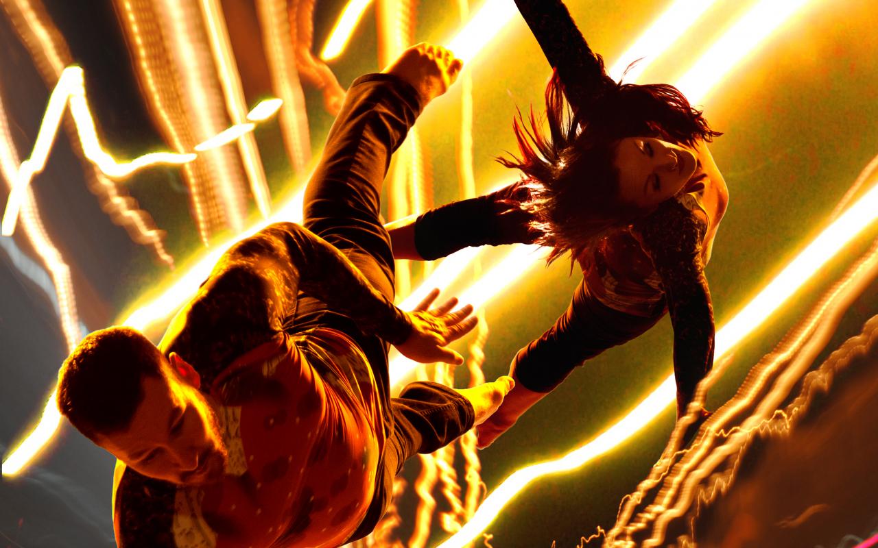 Das Bild zeigt zwei TänzerInnen, die aus einem Licht-Blitz-Gewitter herauszuschweben scheinen. 