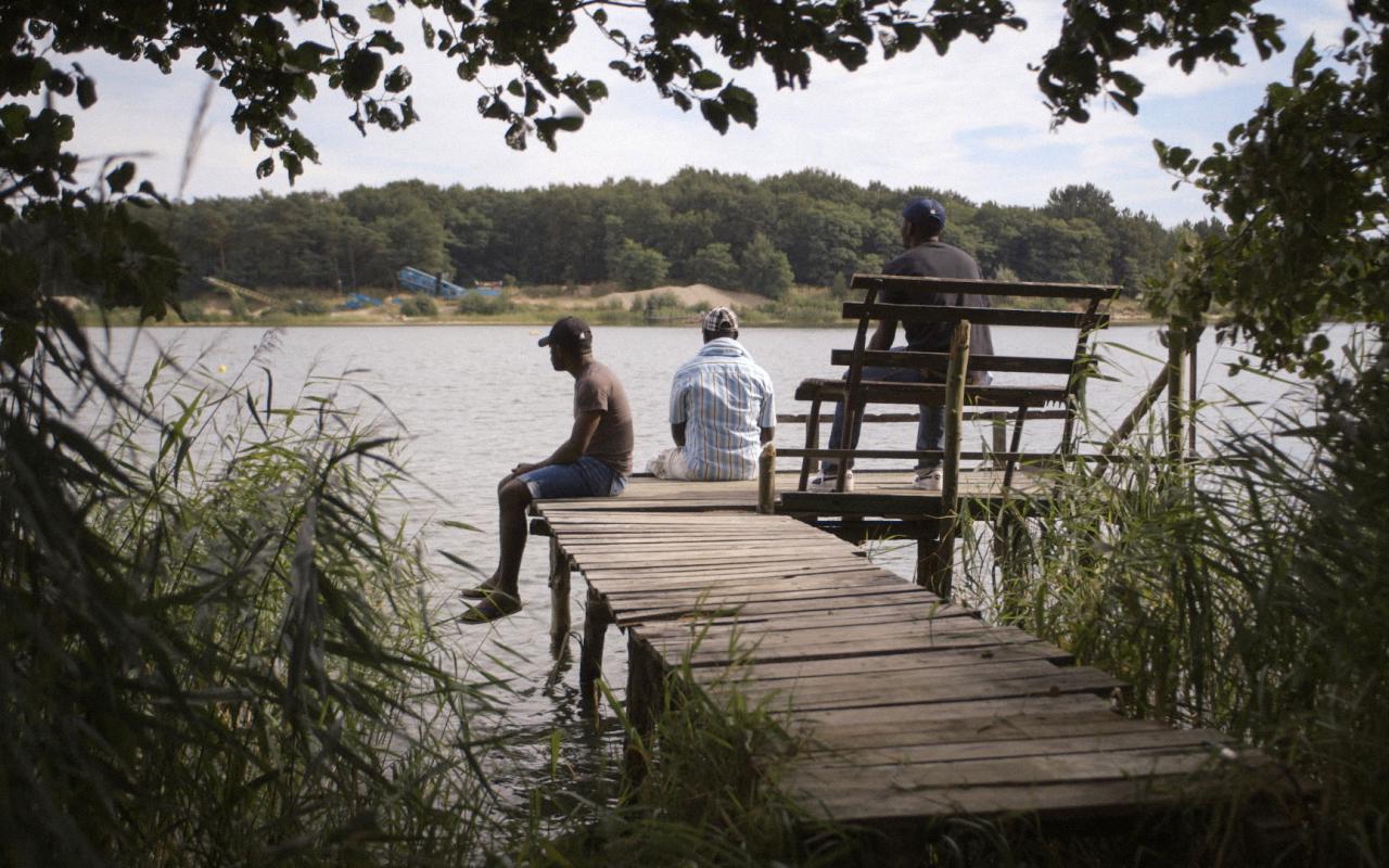 Three men sitting on a pier at a lake