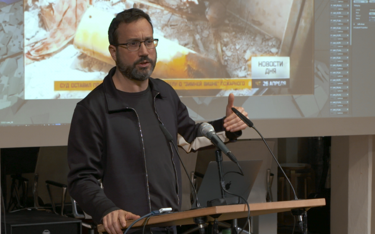 Eyal Weizman, ein Mann mit Bart und Brille hält einen Vortrag vor einer Leinwand..