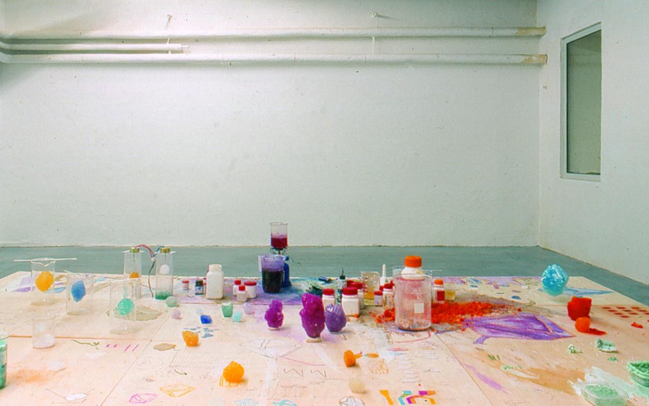 Blick in die Ausstellung »Fiction & Science». Im Vordergrund ein Tisch mit farbigen Kristallen und Chemikalien.