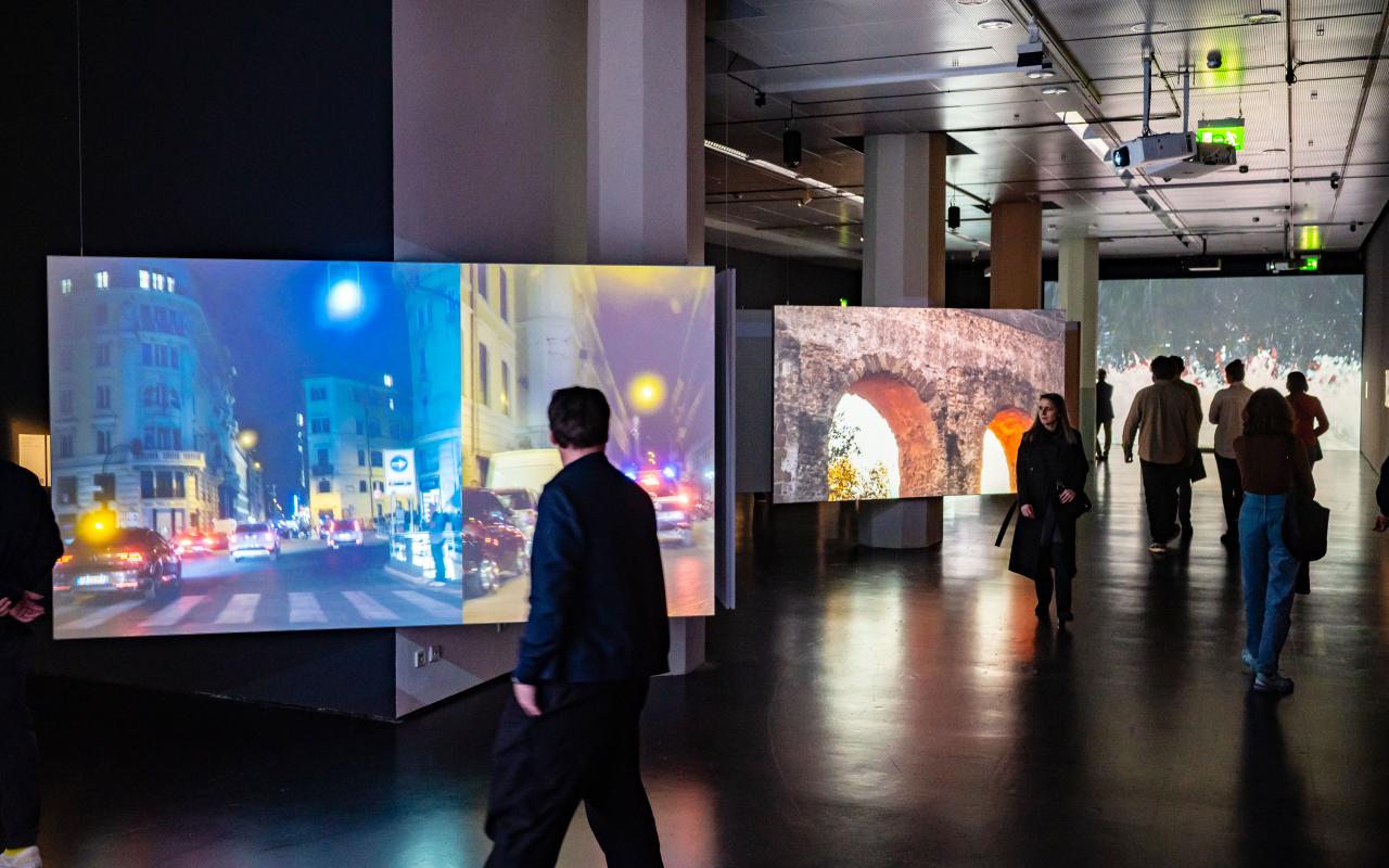 Videos showing views of Rome are projected onto three screens distributed around the room.