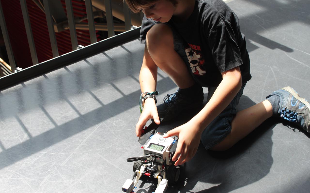 A boy is kneeling on the floor next to a lego-robot.