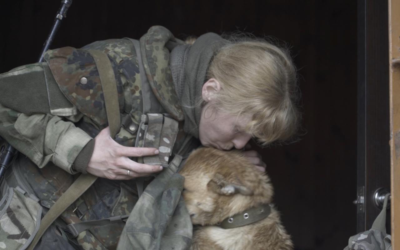The picture shows a woman in camouflage colors caressing her dog.