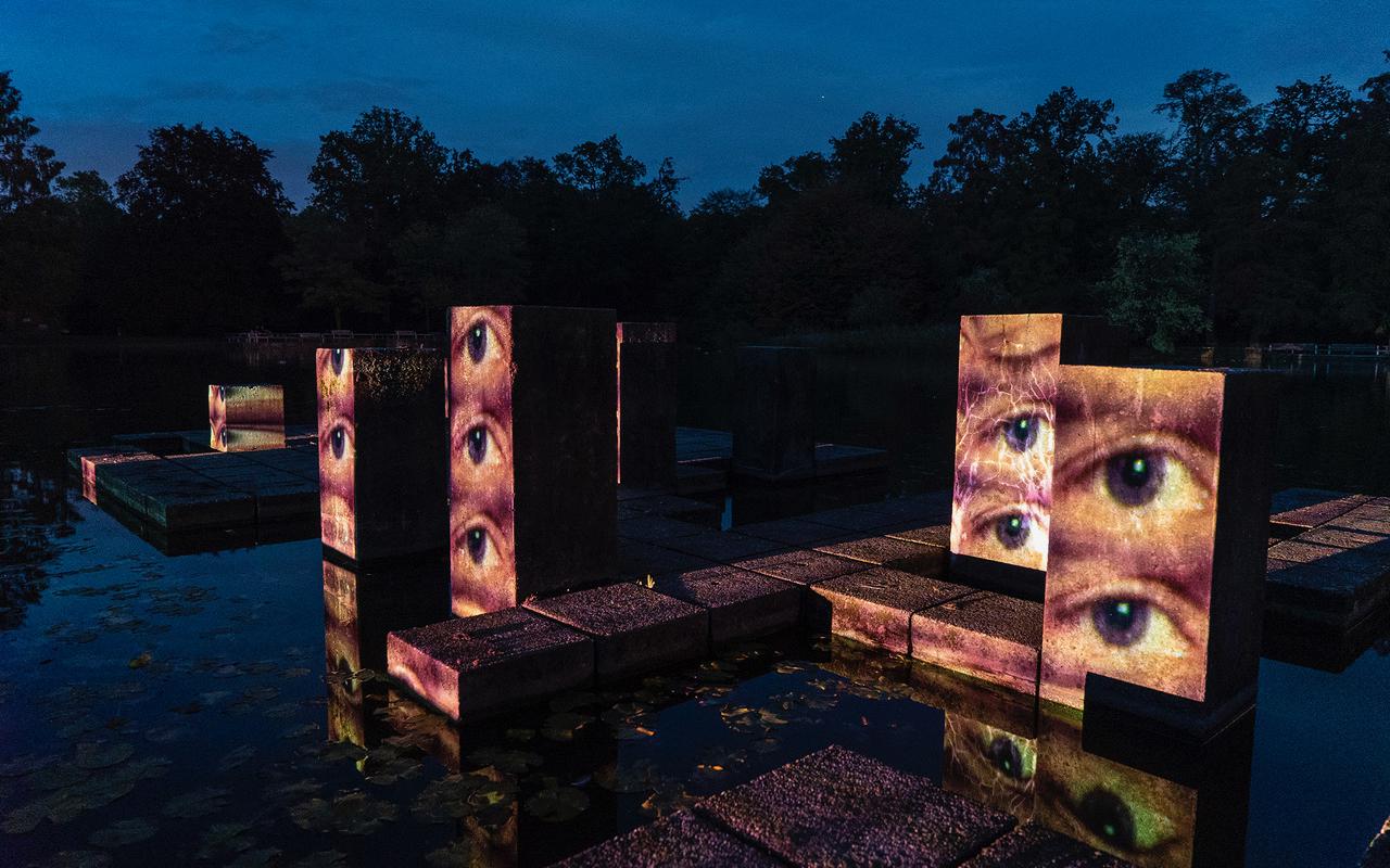Stelae inside a lake in a park. It is late evening. Eyes are mapped onto the stelae, which look openly into the area