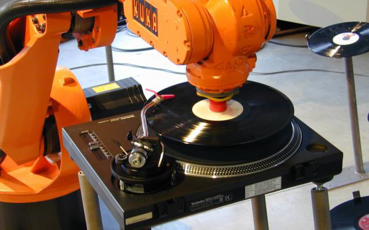 Ein orangener Roboterarm legt Schallplatten auf.