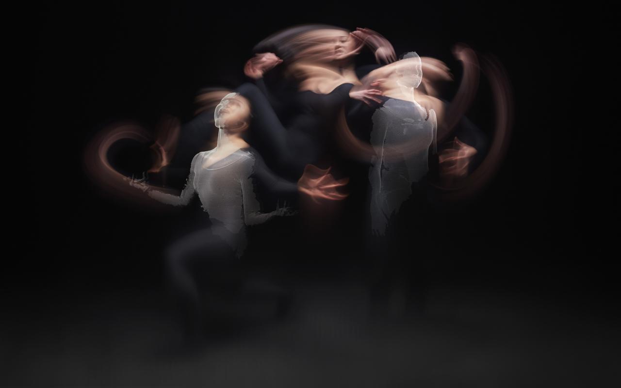 Three dancers are illuminated in a dark room. The bodies are blurred and you don't really know if they are one person or three. Partly computer animated versions of skin protrude from their bodies.