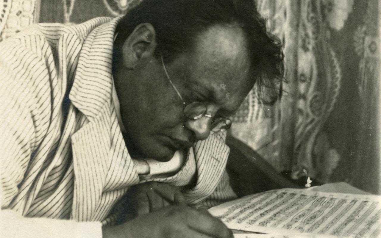 In einer alten schwarz-weiß Fotografie sieht man den Komponisten Max Reger am Tisch gebeugt über Notenblättern sitzen, einen Federhalter in der Hand.
