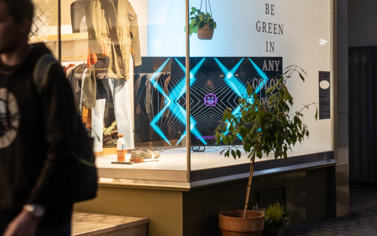 The interactive light installation is shown on a large screen located in the window of a clothing shop.