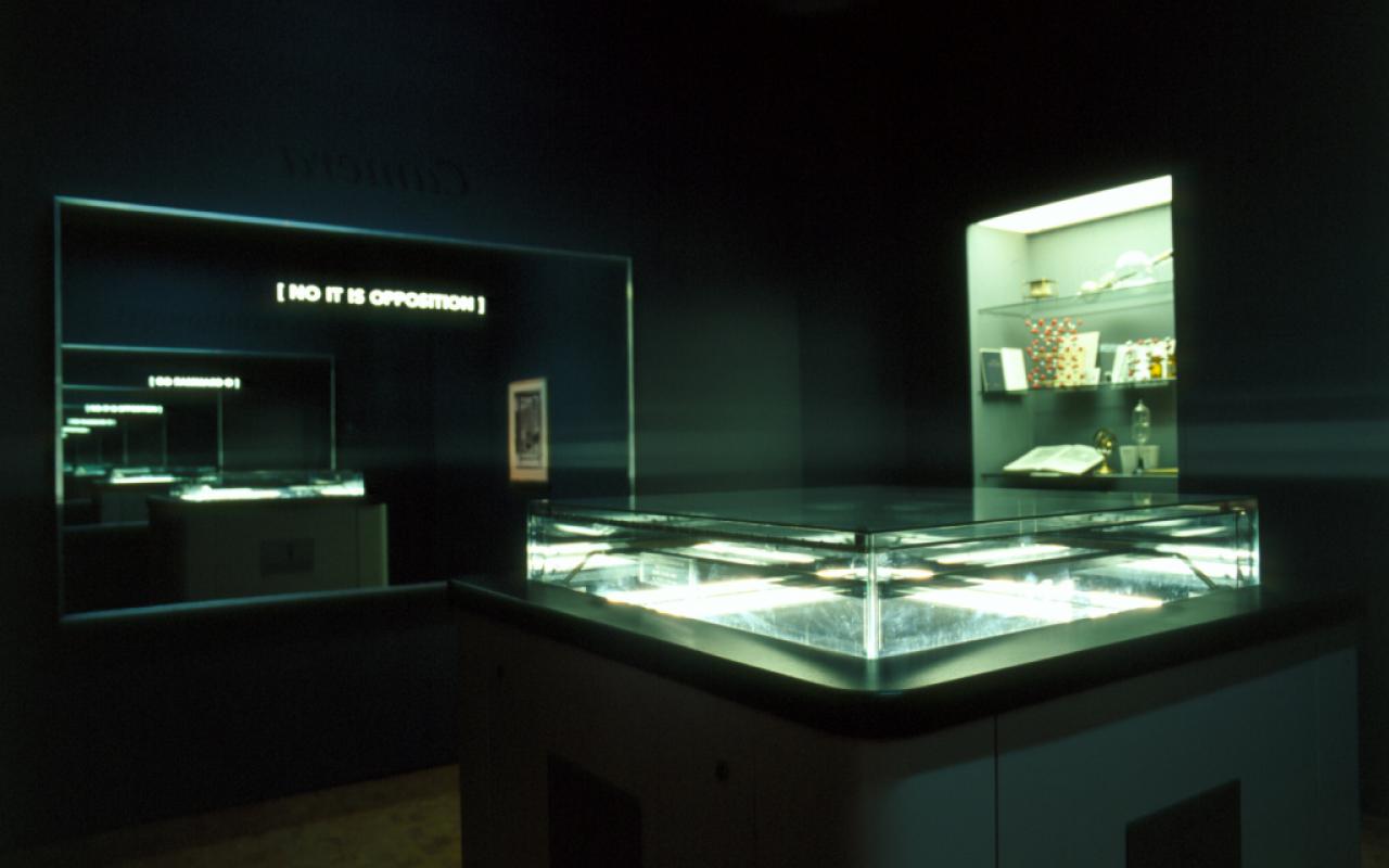 A view of the exhibition »Iconoclash« shows  "the typosophic pavilion"  by Ecke Bonk und Richard Hamilton: a dark room with illuminated showcases and a mirror with the inscription »No It Is Opposition«