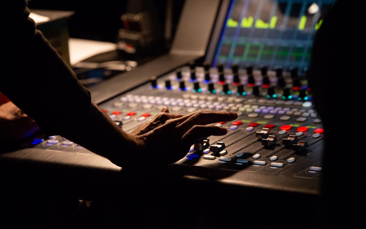 A hand operates a sound mixer in the dark at an event