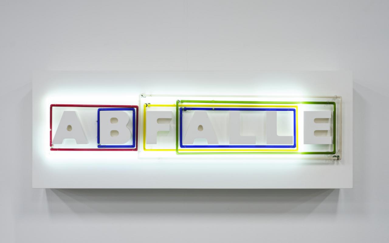 Das Foto zeigt weiße Buchstaben, die das Wort »ABFÄLLE« bilden. Um Buchstabenkombinationen sind Neonröhren in unterschiedlichen Farben und Größen zu sehen. Diese verändern ihre Lichtverhältnisse.