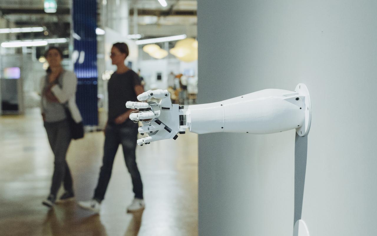 Aus einer Wand ragt eine Roboterarm, dessen Hand etwas umschlossen hält.
