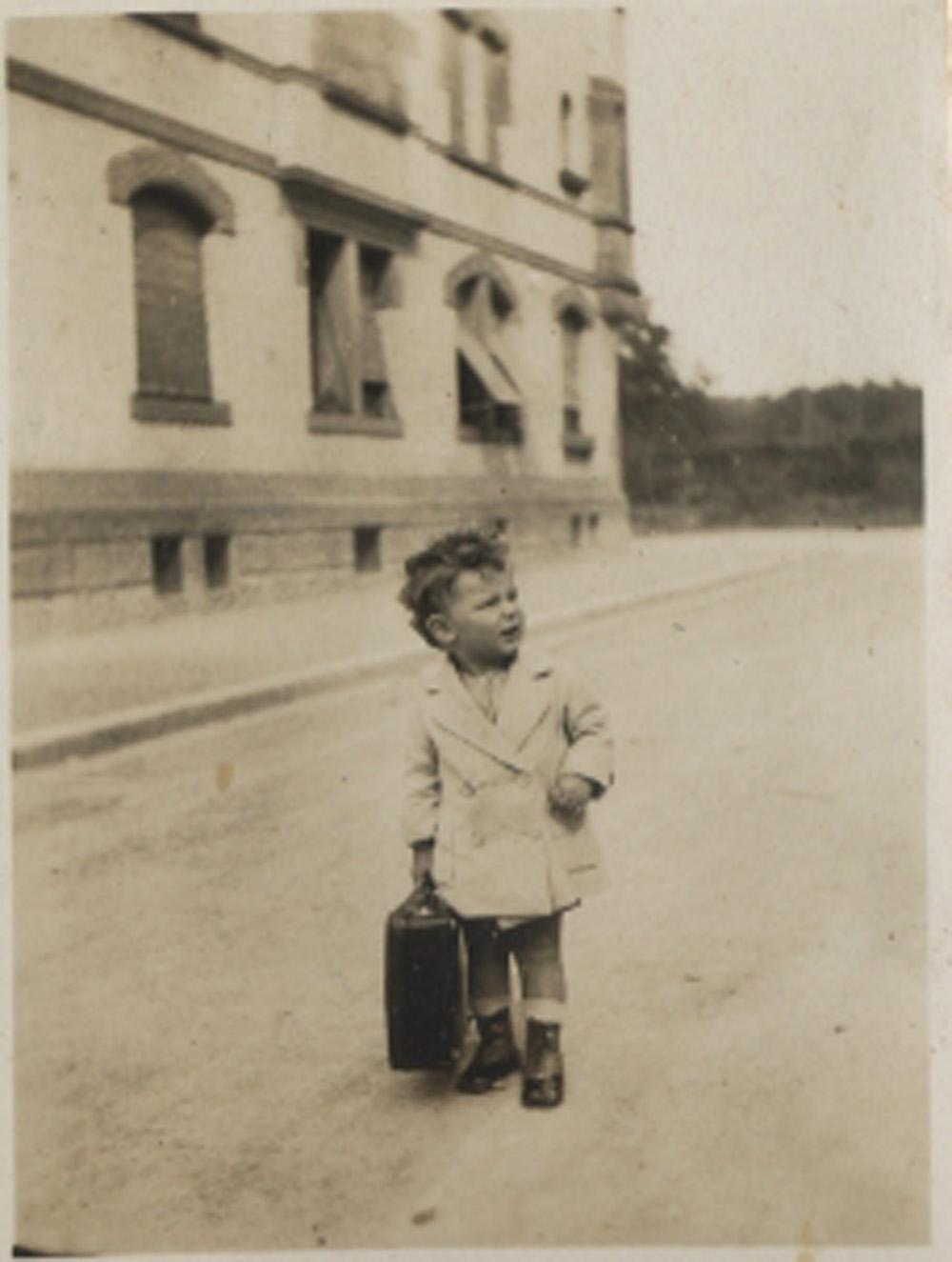 Young boy with suitcase in front of house. 