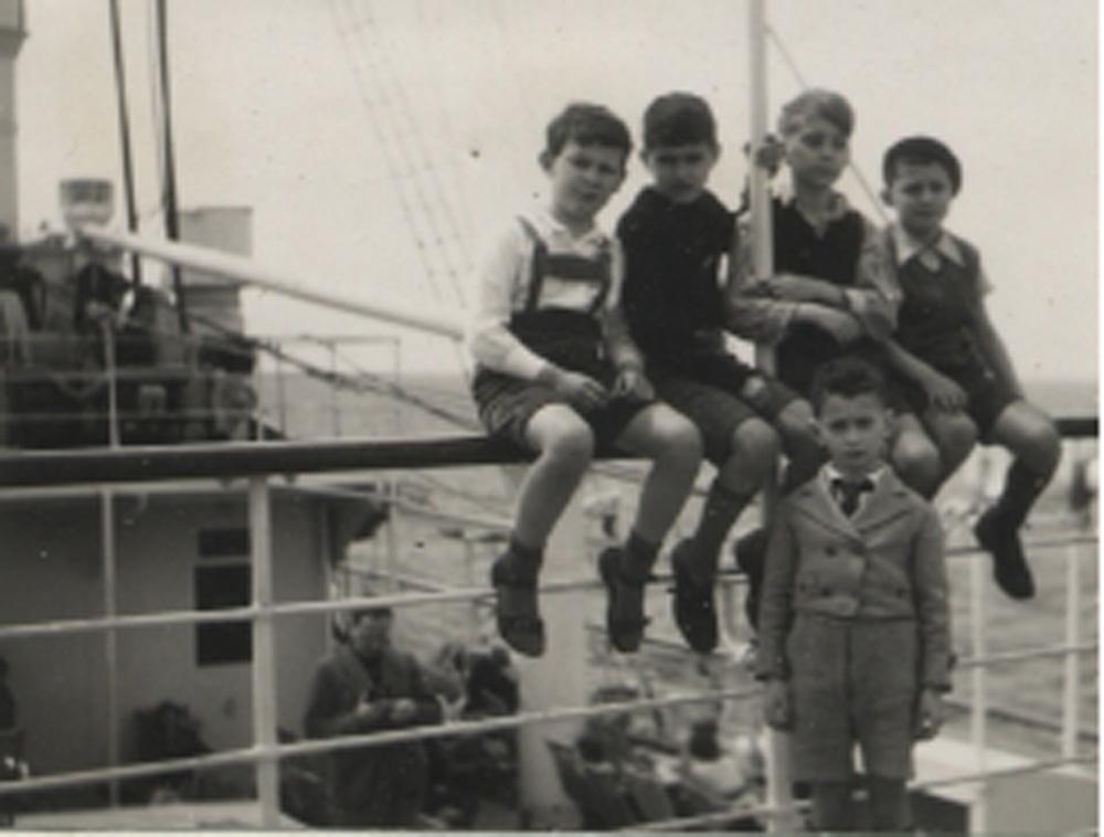 Five boys sitting on railing of ship. 
