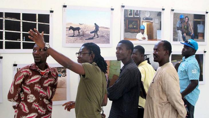 Sechs Männer betrachten Fotografien an der Wand