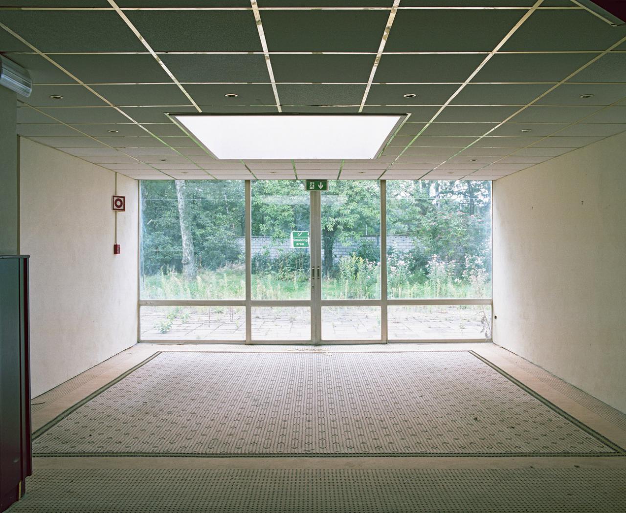 An empty room with large windows overlooking in a leafy outdoor area.