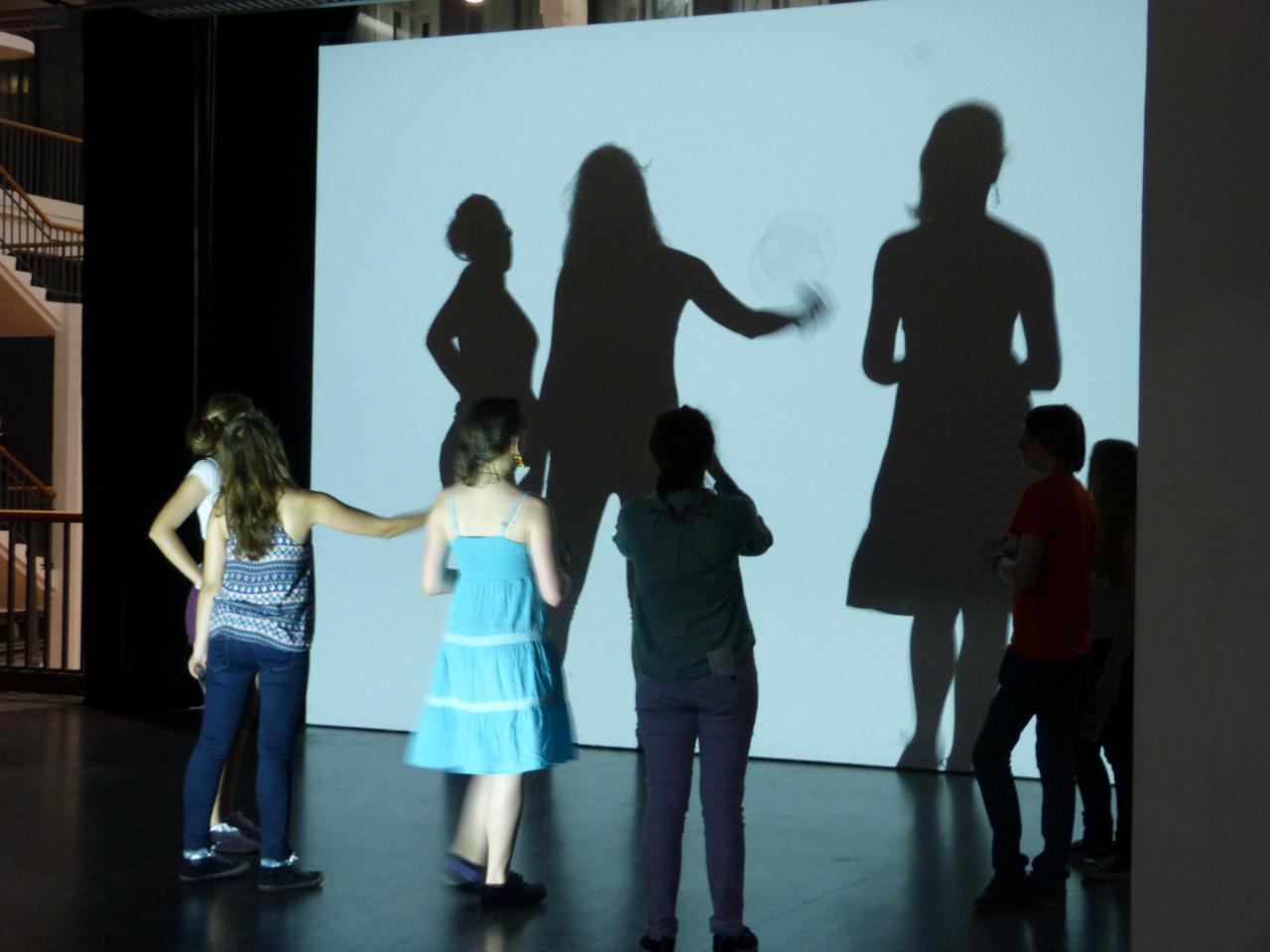 Children are standing in front of a wall where there shadows fall
