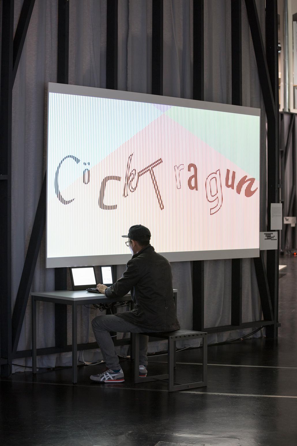 Ein Mann sitzt vor einem PC. Auf der Leinwand über ihm steht "CöcKtragun"