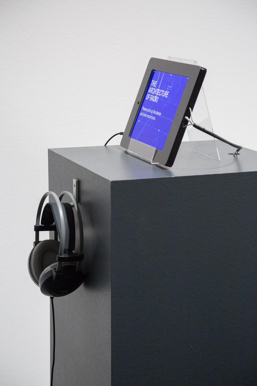 A pedestal on which a tablet stands and headphones hanging
