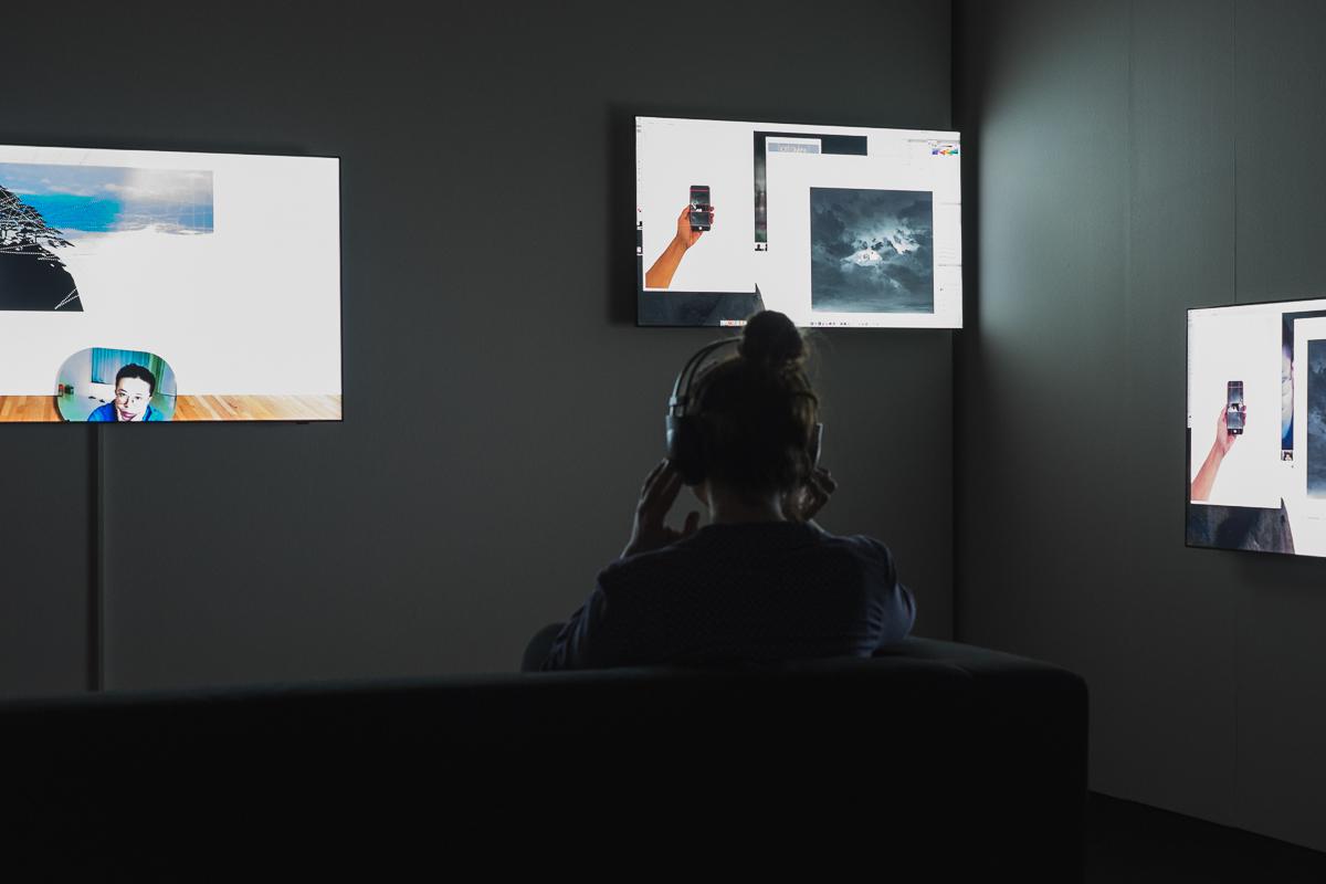 Eine Frau mit Kopfhörern sitzt vor drei Bildschirmen
