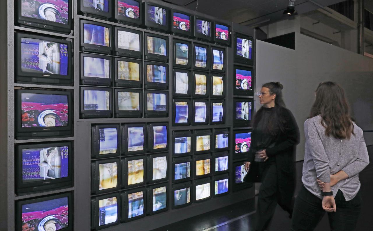 Besucherinnen vor einer Installation aus 52 Monitoren, die eine bunte Bildchoreografie zeigen. 